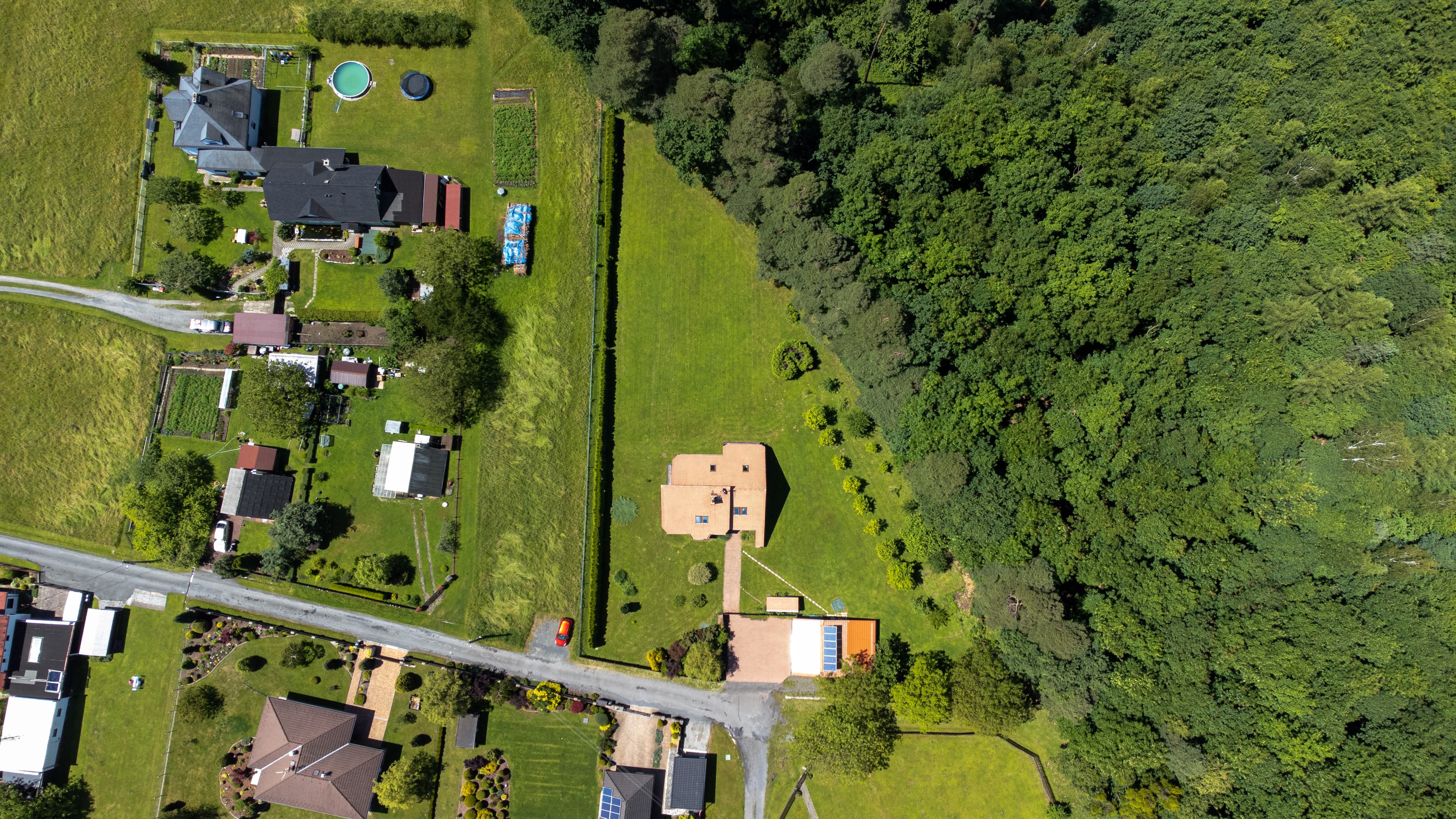 Obrázek z dronu nad rodinným domem s lesem v pozadí.