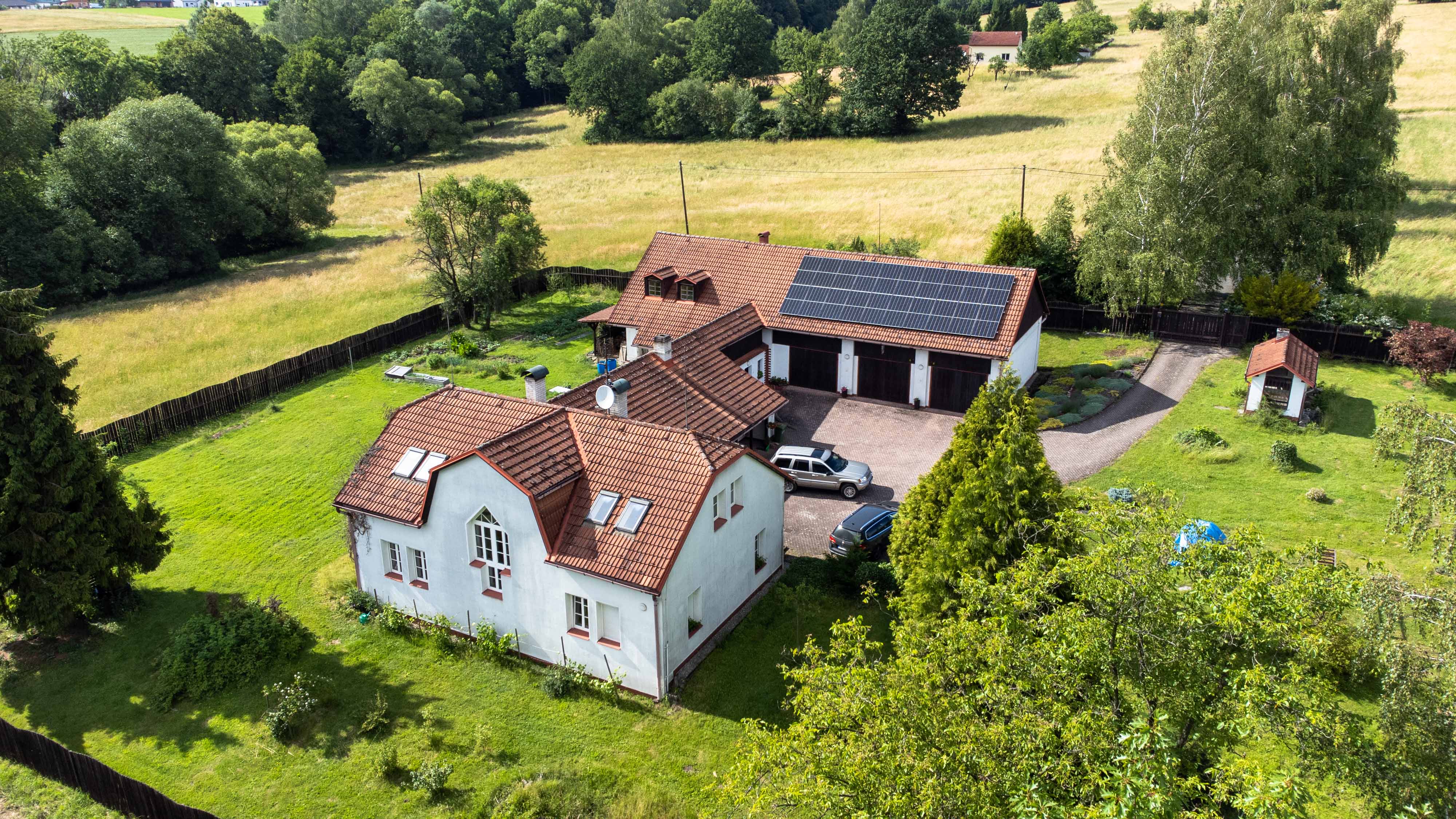 Obrázek z dronu nad rodinným domem s lesem v pozadí.